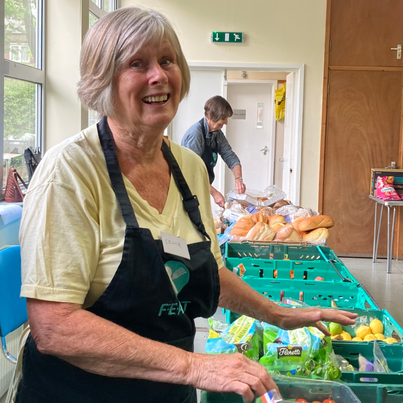 A smiling FEAST volunteer serving salad at a community larder