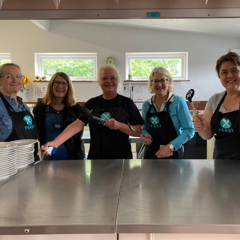 Five smiling FEAST volunteers ready to serve lunch