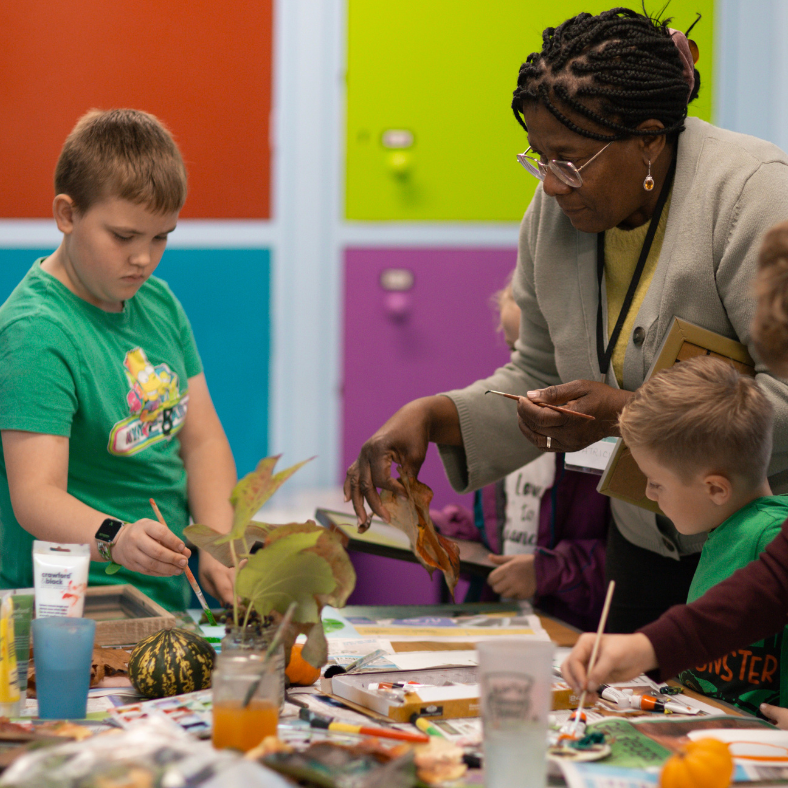 Two young boys doing craft with leaves with the help of a lady volunteer