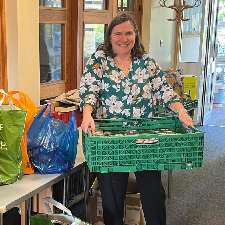 Lady carrying a green crate of tins to donate