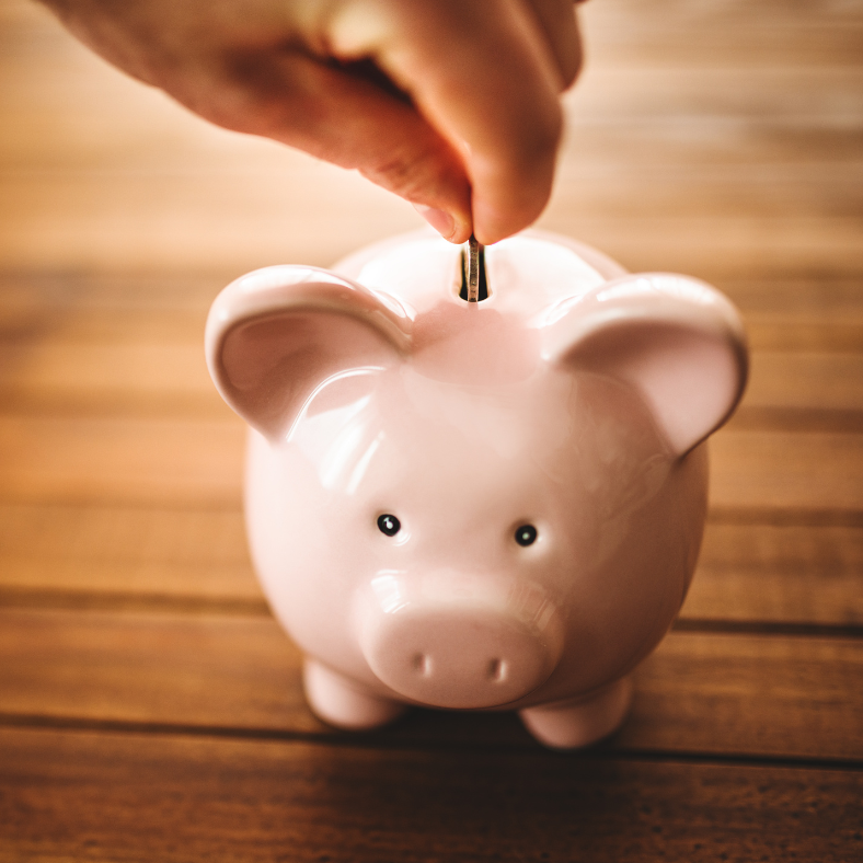 Hand placing a coin into a pink piggy bank