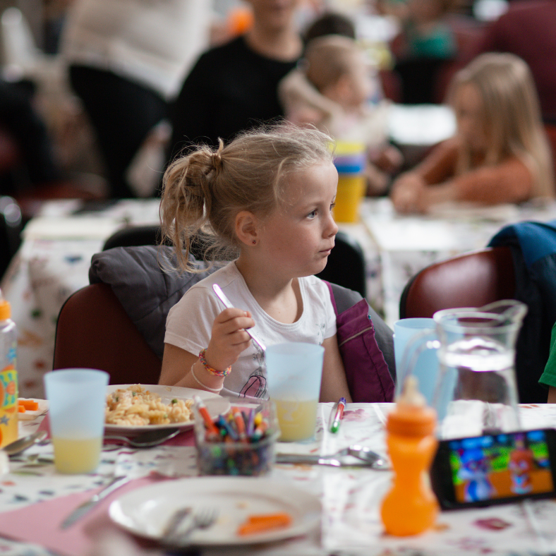 Child eating a meal alongside other children and families.