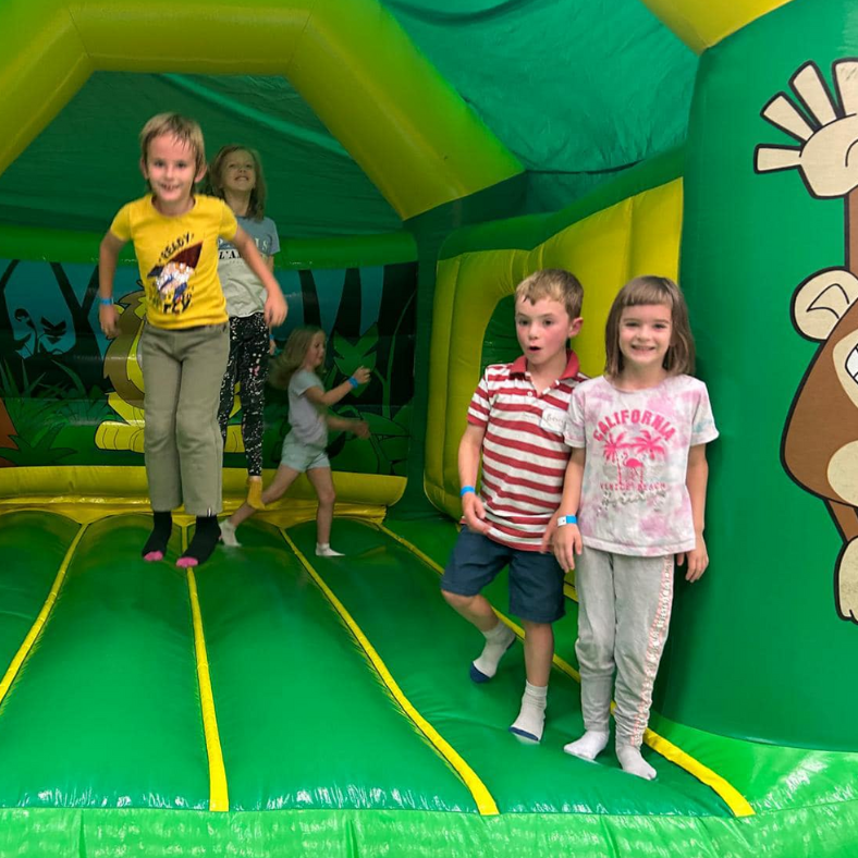 Three children bouncing on a green bouncy castle